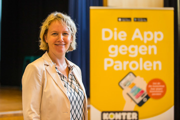 Frau Engler vor dem Roll-Up "Die App gegen Parolen"