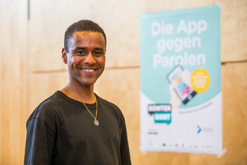 Moderator Tarik Tesfu vor dem Plakat "Die App gegen Parolen"