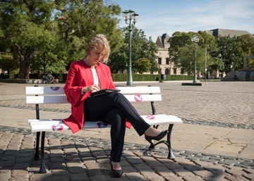 Frau Engler sitzt mit einem Tablet auf einer Bank auf dem Opernplatz in hannover
