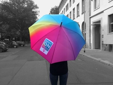 Eine Person steht mit einem bunten Spot on-Regenschirm auf der Straße