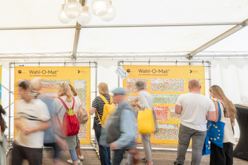 Viele Menschen vor zwei gelben Planen des Wahl-O-Mat zum Aufkleben zur Europawahl