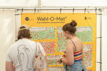 Zwei Personen mit Klebepunkten vor einer Plane mit Thesen vom Wahl-O-Mat zur Europawahl 2024