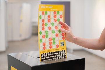 Hand steckt den Klebepunktflyer in den Wahl-O-Mat zum Aufkleben Scanner