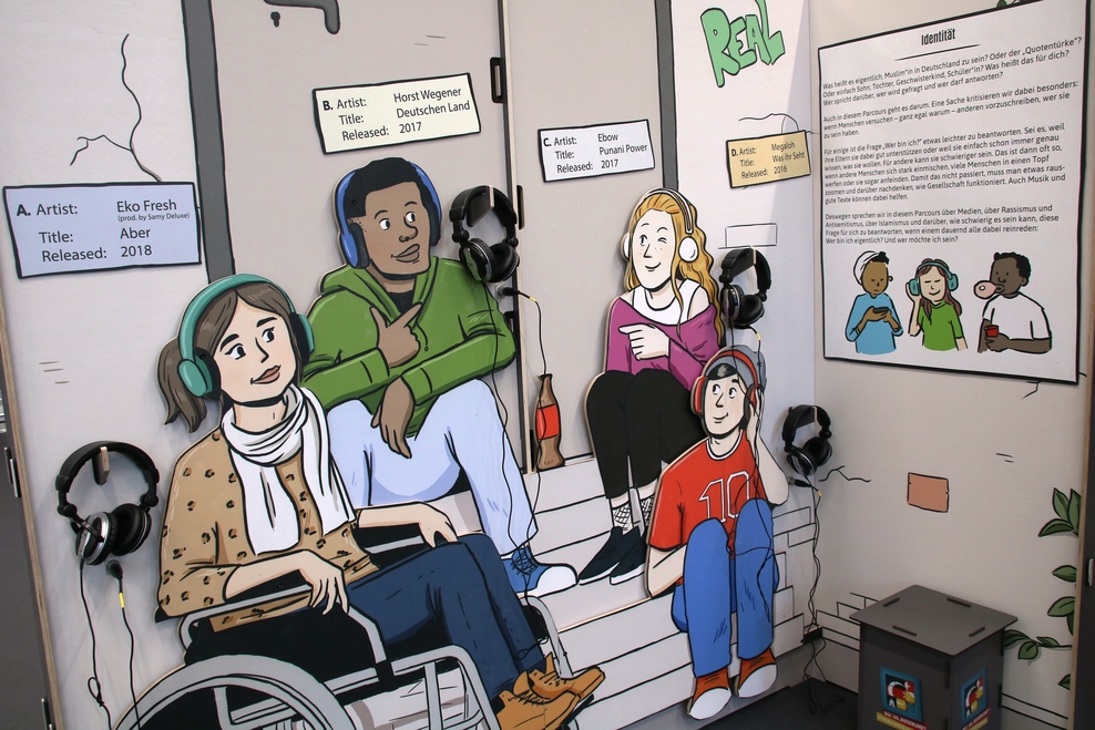 Bild aus der Ausstellung: eine Hörstation an der vier Figuren gemeinsam auf einer Treppe sitzen.